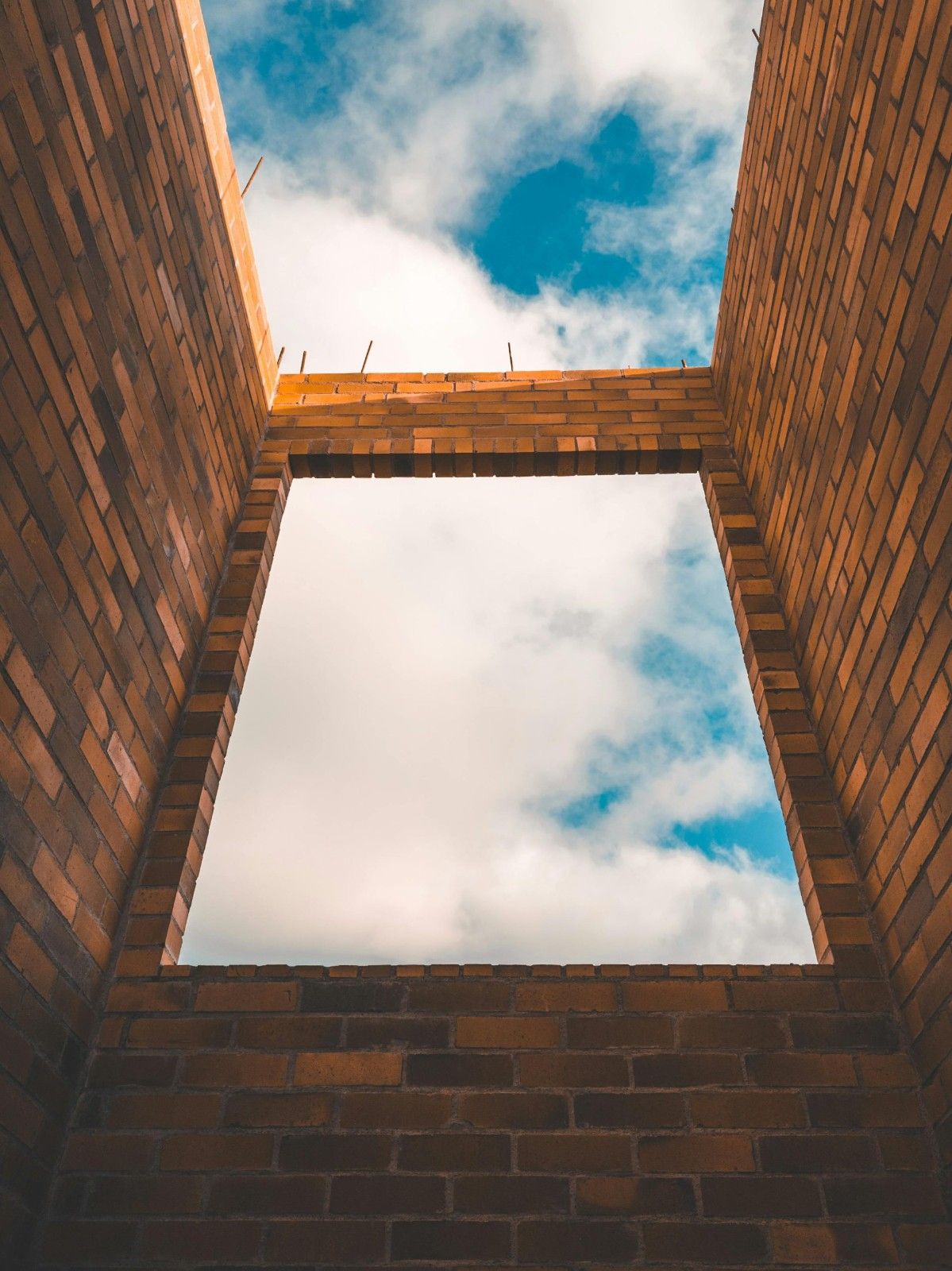 Low-angle view of an unfinished brick structure framing the cloudy sky.